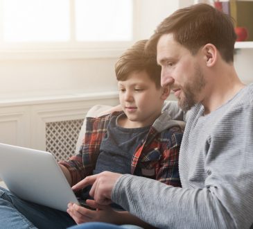 Happy father and son spending time together and surfing internet while sitting on sofa at home