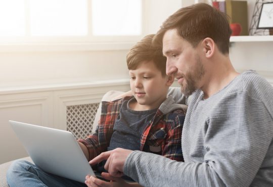 Happy father and son spending time together and surfing internet while sitting on sofa at home