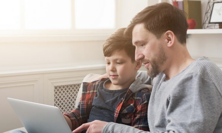 Happy father and son spending time together and surfing internet while sitting on sofa at home
