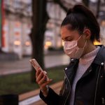 Side view of young woman with face protective mask in a city at dusk