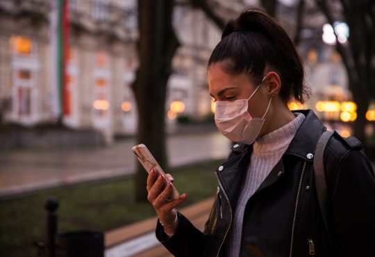 Side view of young woman with face protective mask in a city at dusk