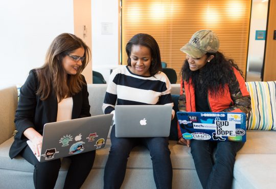 three women using laptops on couch