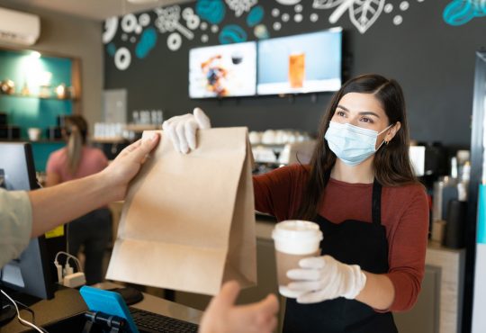 Young female staff giving parcel and coffee to customer at takeaway counter in coffee shop