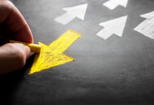 person drawing yellow arrow on chalk board pointing away from white arrows