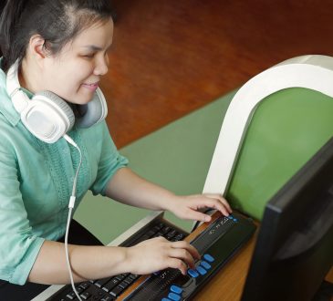 Woman with visual impairment wearing headphones using computer with refreshable braille display