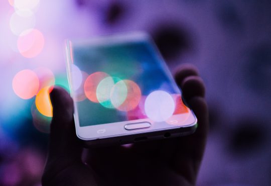 person holding up cellphone with coloured lights shining on screen