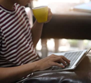 Cropped image of creative man drinking a coffee and using/typing on laptop