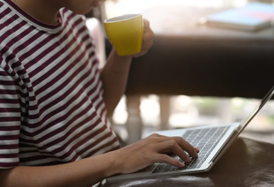 Cropped image of creative man drinking a coffee and using/typing on laptop