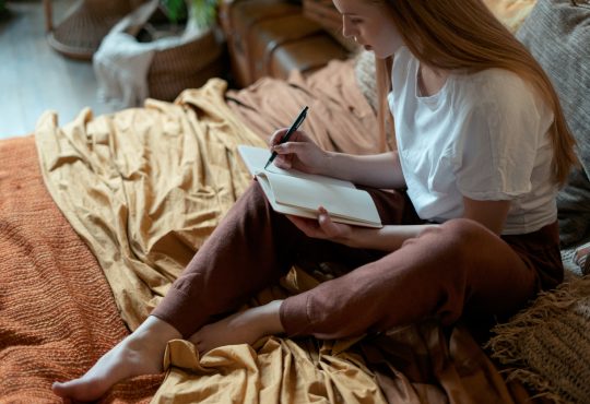 woman writing in journal on bed