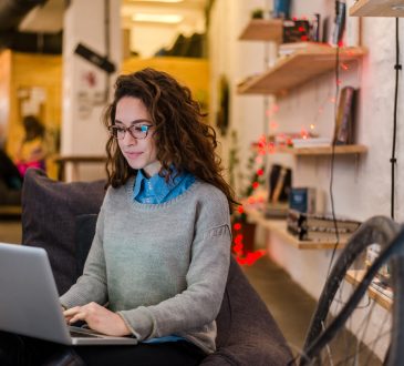 young woman sitting on bench in office working on laptop