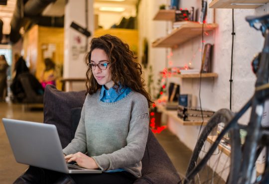 young woman sitting on bench in office working on laptop