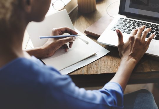 woman holding pencil in one hand with other hand hovering over laptop keyboard