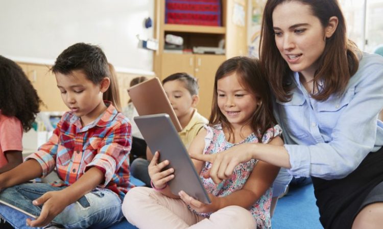 teacher sitting with young students on classroom floor