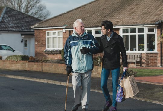 young man helping old man carry groceries