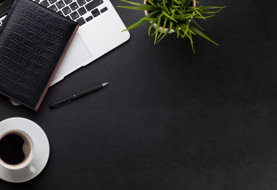 Office leather desk workplace table with laptop, coffee cup, notepad and plant.