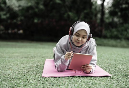 student lying on grass looking at tablet