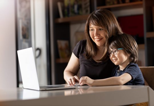 Mother and boy studying with laptop in home.