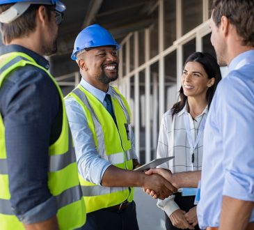 Smiling engineer shaking hands at construction site with happy architect.
