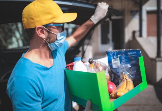 Delivery guy with protective mask and gloves delivering groceries during lockdown and pandemic.