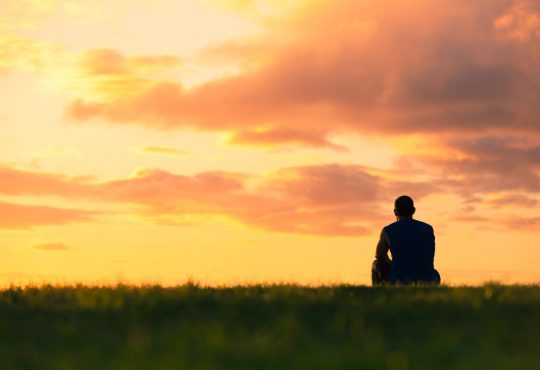 man sitting in field watching sunset