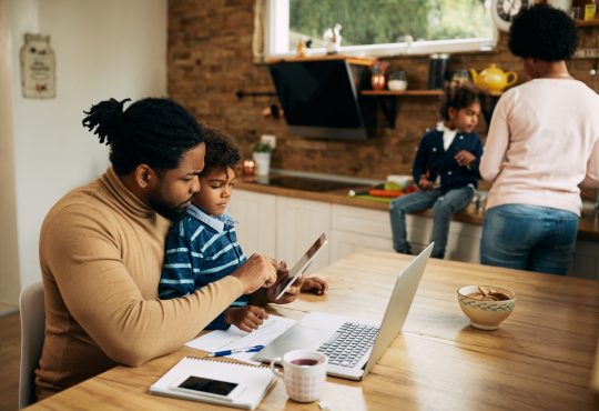 man sitting at kitchen table working with son in lap