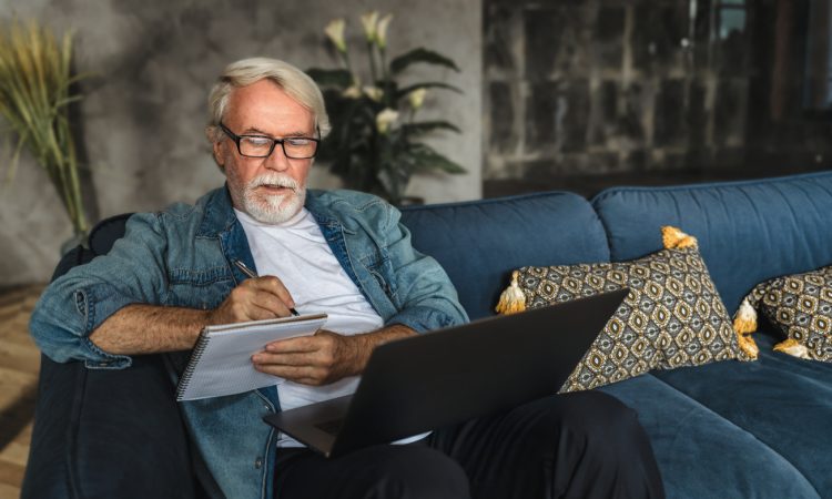 older man writing notes in notebook watching webinar
