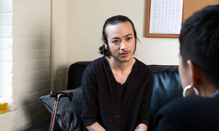 A genderqueer person sitting on a couch talking to a counsellor