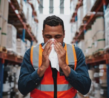 Warehouse worker blowing nose while working wearing safety vest