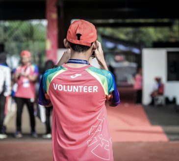 man wearing shirt with "volunteer" on the back taking photo at outdoor event