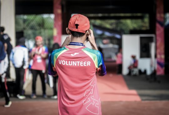 man wearing shirt with "volunteer" on the back taking photo at outdoor event