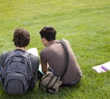 two male students with homework sitting on grass