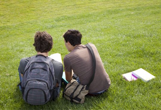 two male students with homework sitting on grass