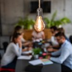 light bulb glowing over office meeting at table