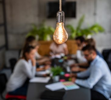 light bulb glowing over office meeting at table