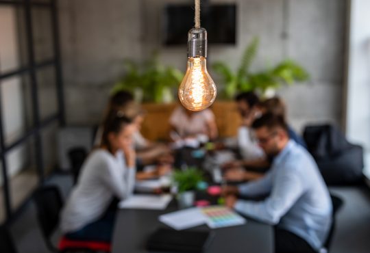 light bulb glowing over office meeting at table