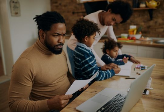 dad working while mom homeschools kids at kitchen table