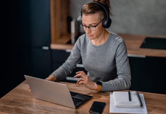 Focused woman wearing headphones, watching a webinar and writing notes.