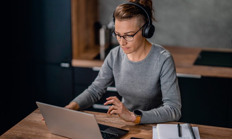 Focused woman wearing headphones, watching a webinar and writing notes.