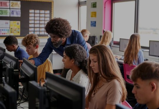 male teacher helping high school students in computer lab