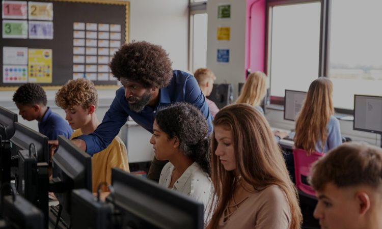 male teacher helping high school students in computer lab