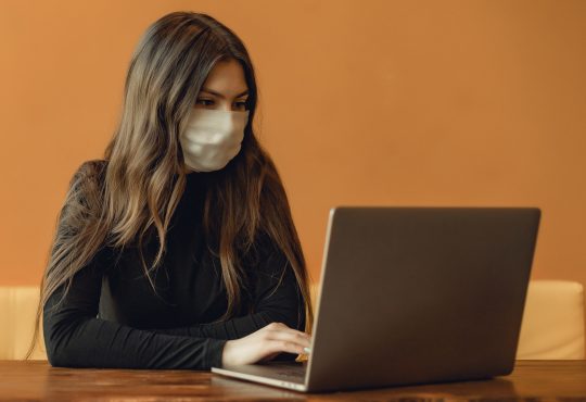 woman wearing mask typing on laptop