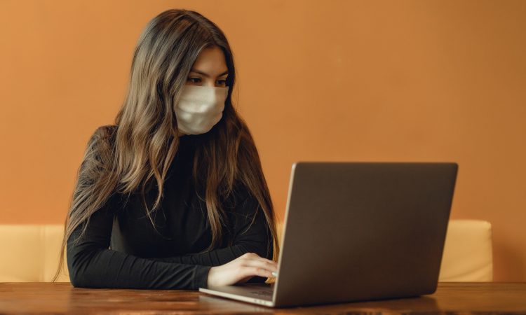 woman wearing mask typing on laptop