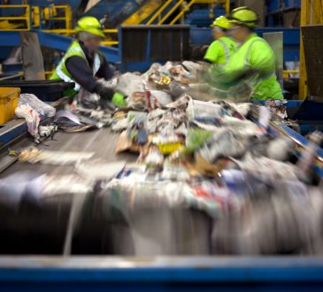 Workers separating paper and plastic on a conveyor belt in a recycling facility