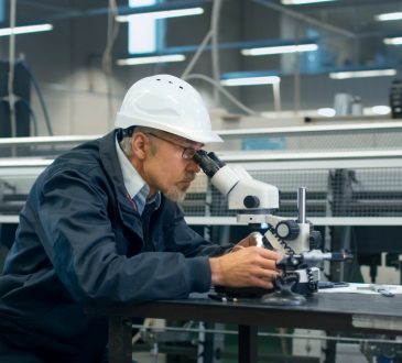Senior engineer is inspecting a detail under microscope in a factory.