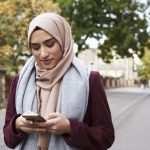 woman wearing hijab walking outside and texting