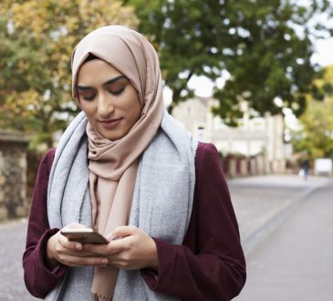 woman wearing hijab walking outside and texting