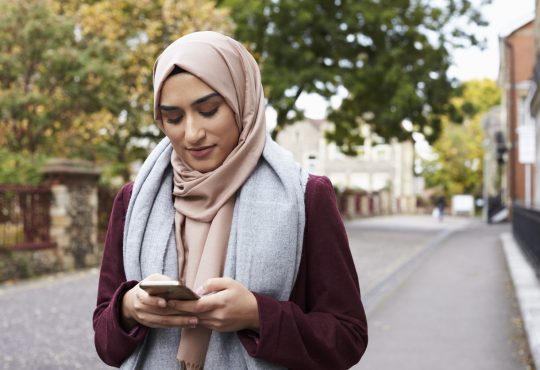 woman wearing hijab walking outside and texting