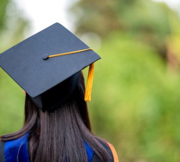 closeup behind a female college graduate wearing a black fringe gown and a black hat,