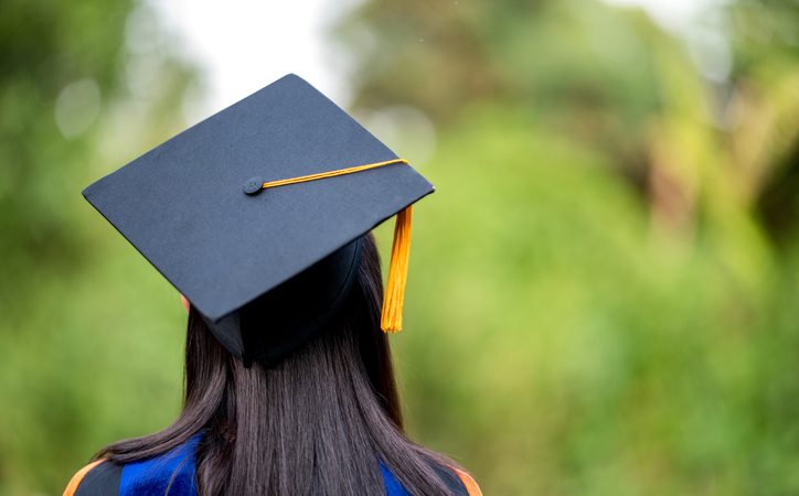 closeup behind a female college graduate wearing a black fringe gown and a black hat,