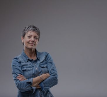 Confident senior woman with folded arms standing looking at camera with a thoughtful quiet smile over grey with copy space
